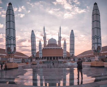 Tourists at temple against sky during sunset