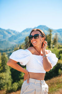 Young woman wearing sunglasses standing against mountain