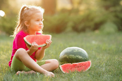 Funny cute child girl 3-4 year old eating ripe watermelon on green grass outdoor. 