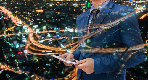 Double exposure of businessman with digital tablet and illuminated cityscape