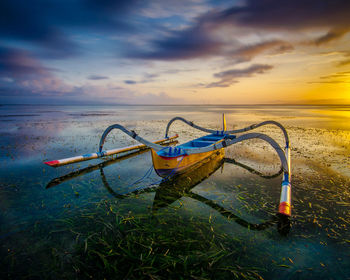 Fishing boat on beach against sky during sunset