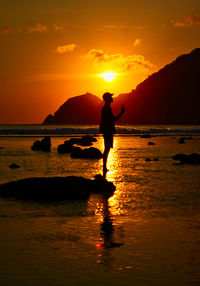 Silhouette man standing on beach against sky during sunset