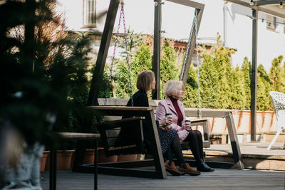 Woman sitting on bench against plants