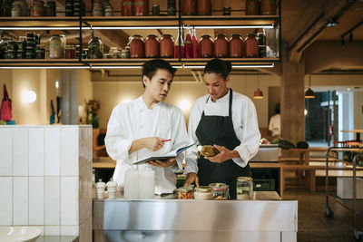 Focused male and female chef discussing while taking inventory while standing in commercial kitchen
