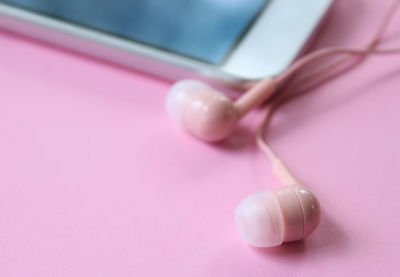 Close-up of in-ear headphones and smart phone on pink table