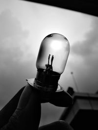 Low angle view of hand holding light bulb against sky