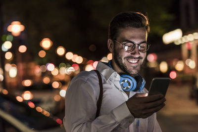 Smiling young man in the city checking cell phone at night
