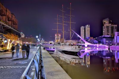 Sailboats moored on river by buildings against sky at night