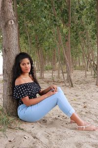 Portrait of young woman sitting by tree trunk at beach