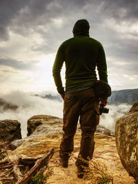 Photographer on mountain cliff looking into mist. hiker will take picture with small camera in hands