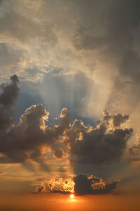 Low angle view of sunlight streaming through clouds during sunset