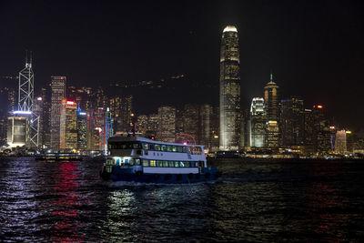 Illuminated buildings by sea against sky at night