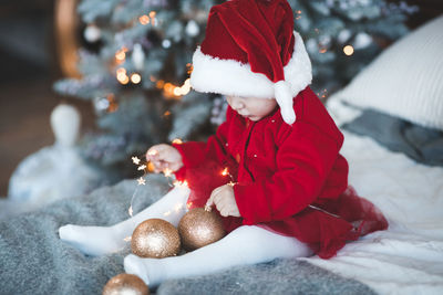 Cute girt wearing santa costume sitting on bed at home