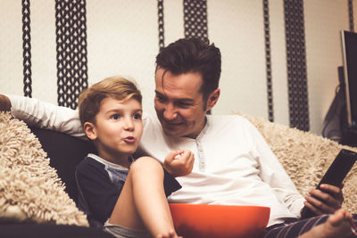 Father and son eating popcorn while watching movie at home