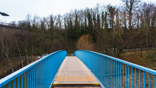 Footbridge over river amidst trees in forest against sky