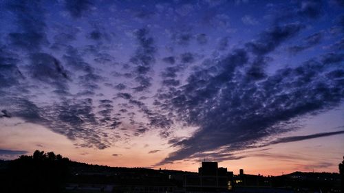 Silhouette of buildings against cloudy sky at sunset