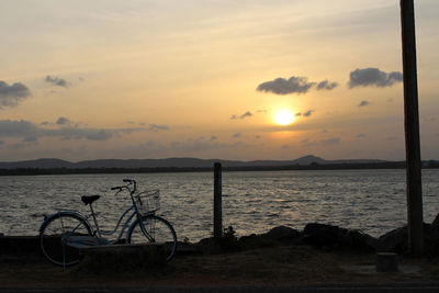 Bicycle by sea against sky during sunset
