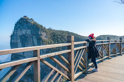 Woman standing on footbridge against clear sky