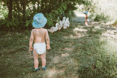 Rear view of shirtless boy standing on grassland