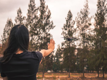 Rear view of woman gesturing towards drone against trees