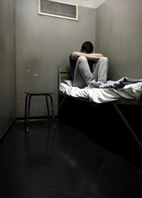 Male prisoner sitting on bed in prison