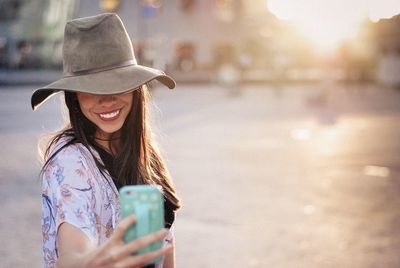 Happy woman taking selfie from mobile phone on street in city during sunset