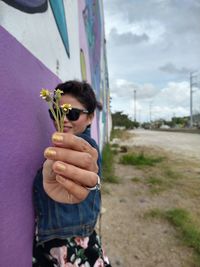 Full length of girl holding flower standing against wall