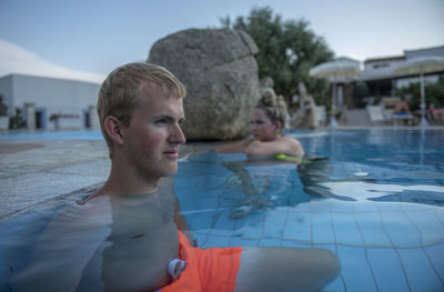 Portrait of young man in swimming pool with girl in the background