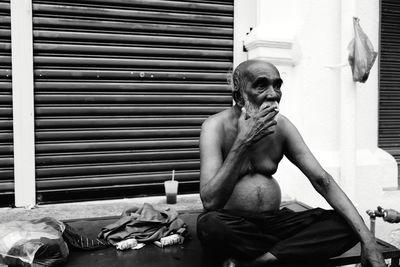 Portrait of shirtless man sitting on window