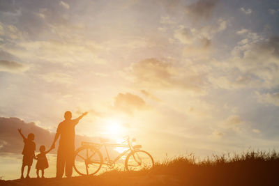 Silhouette people on bicycle against sky during sunset