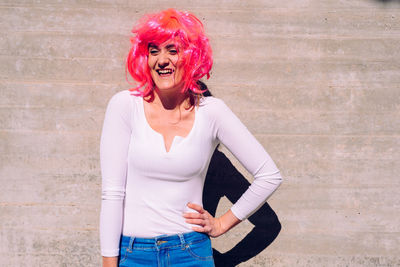 Happy woman wearing wig while standing against concrete wall