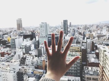 Cropped image of person by buildings in city against sky