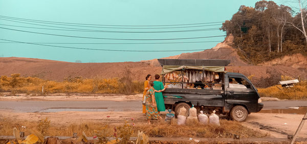 People standing by motor van on road against sky