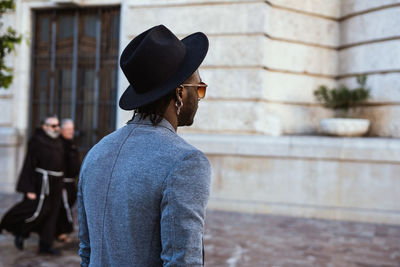 Rear view of man wearing hat standing against wall