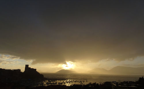 Silhouette buildings by sea against sky during sunset