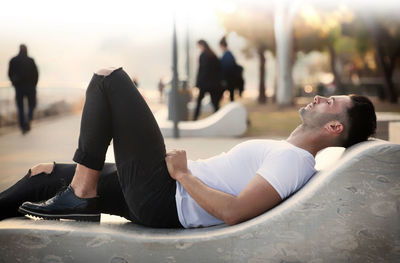 Side view of man relaxing on sculpture at park