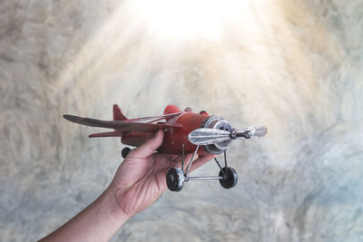 Cropped hand of woman holding toy airplane against wall