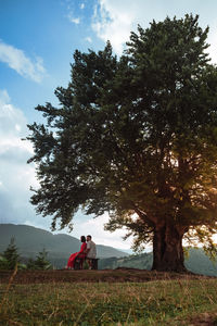 Rear view of woman sitting on field against sky