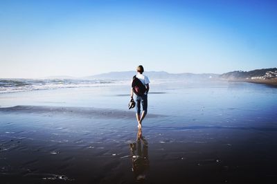 Man walking on beach against clear sky