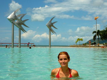 Portrait of smiling young woman in swimming pool against sky