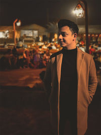 Portrait of young man standing against illuminated lantern in the backdrop of a celebration