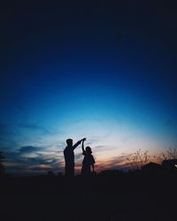 Silhouette friends standing on golf course against sky during sunset