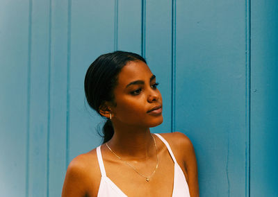 Beautiful young woman looking away while standing against wall