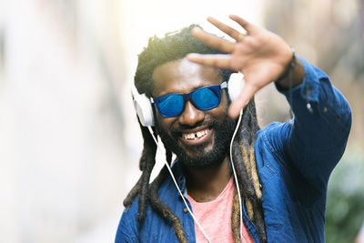 Smiling young man wearing sunglasses listening music on headphones in city