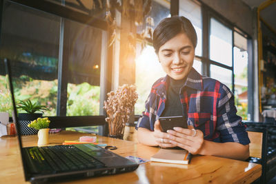 Young woman using phone while sitting on table
