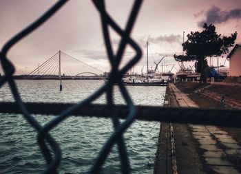 Chainlink fence by bridge against sky