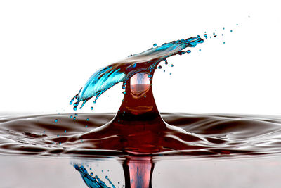 Close-up of drop falling on water against white background