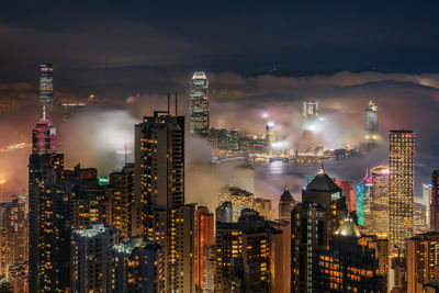 Illuminated modern buildings in city against sky at night