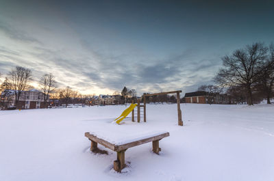 Snow covered field by trees against sky during winter