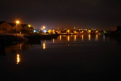 Illuminated city by sea against sky at night